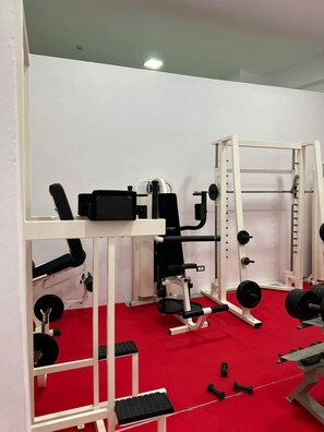 Een sportschool met gewichthefapparatuur, banken en een vloer van rood tapijt.