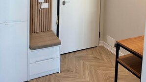 A room with a white door, a bench with a cushion, a small table, and a wall-mounted electrical box. - Valerie - Corfu View Residence (Sarandë)