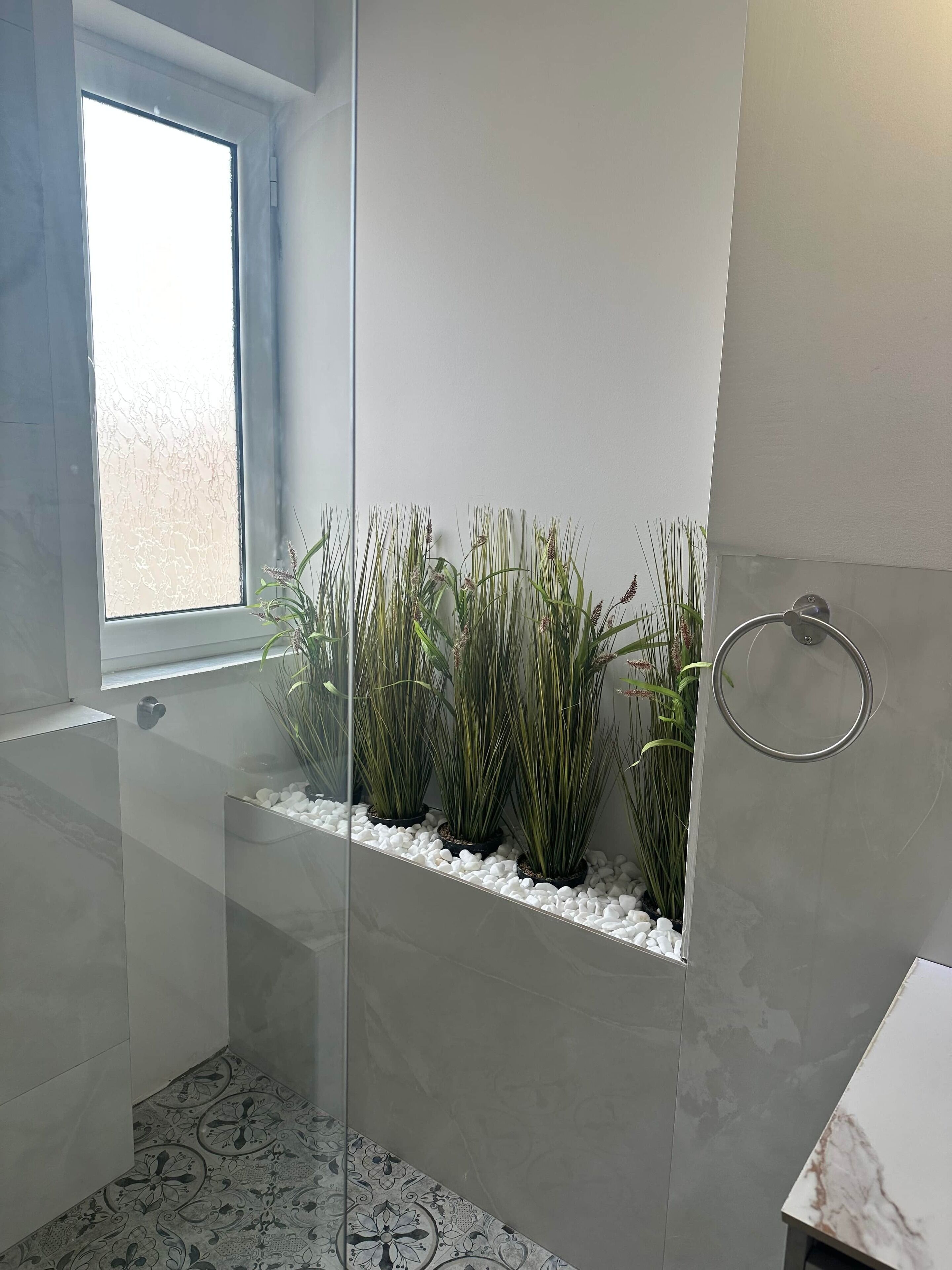 A modern bathroom with a glass shower enclosure, a window, and a built-in planter with plants.