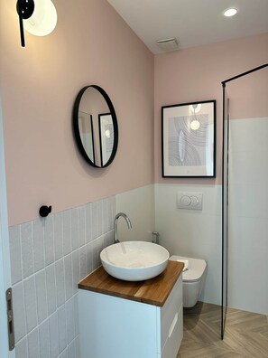 A modern bathroom with a round mirror, a framed abstract artwork, a white sink, and a toilet. - Vanessa - Corfu View Residence (Sarandë)