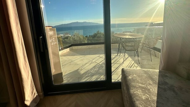 Un balcon avec une table et des chaises, une vue sur la mer et une chaîne de montagnes à l’horizon.