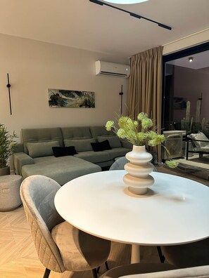 A modern living room with a grey sofa, a round white table, and a vase with green plants. - Vespera Horizon Suite- Adults Only (Sarandë)