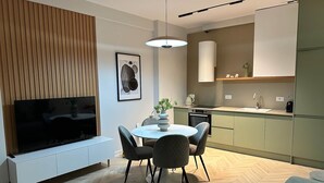 Un salon moderne doté d’un téléviseur à écran plat, d’une table de salle à manger ronde avec quatre chaises et d’un mur décoratif en bois.