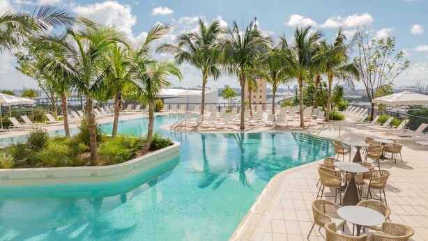 A pool area with lounge chairs, palm trees, and a view of the cityscape.