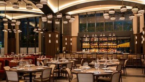 A restaurant with round tables, chairs, and a bar area with shelves of bottles.