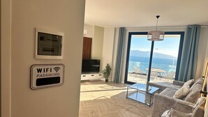 A modern living room with a herringbone floor, a sofa, a coffee table, and a large window offering a view of the sea. - Vivien - Corfu View Residence (Sarandë)