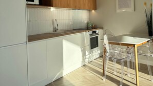 A modern kitchen with white cabinetry, a wooden upper shelf, a microwave, and a stove. - Vivien - Corfu View Residence (Sarandë)