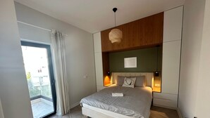 A modern bedroom with a bed, bedside lamps, a view through a sliding door, and a ceiling light fixture. - Vivien - Corfu View Residence (Sarandë)