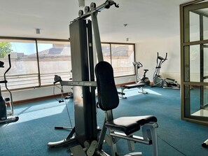 Ein Fitnessstudio mit verschiedenen Trainingsgeräten, darunter eine Bank, ein Kraftgerät und Cardiogeräte.
