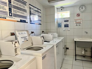Eine Waschsalon mit mehreren Waschmaschinen und Trocknern, einer Uhr und Informationsplakaten an den Wänden.