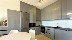 Une cuisine moderne dotée d’appareils électroménagers en acier inoxydable, un coin repas avec une table et des chaises blanches, et un four encastré.