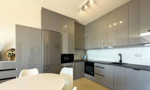 Eine moderne Küche mit Edelstahlgeräten, eine Essecke mit weißem Tisch und Stühlen sowie ein Einbauofen.
