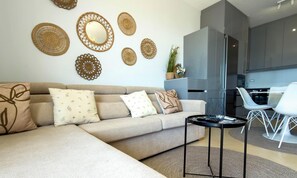 Ein modernes Wohnzimmer mit Sofa, Wanddekorationen, einem kleinen Tisch und einer Küchenzeile mit Esstisch.