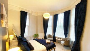 A modern bedroom with a large bed, a desk, a chair, and a hanging light fixture. - 2A Redcliffe (Torquay)