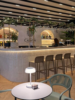 Zona de bar con mostrador, sillas, una mesa con lámpara y un letrero que dice 'The Calaya'.