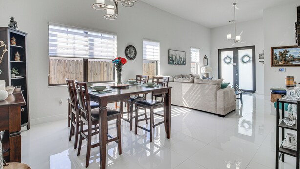 Un grand espace de vie comprenant une table à manger, des chaises et un canapé. On y trouve également un lustre, une horloge et une fenêtre avec des stores.