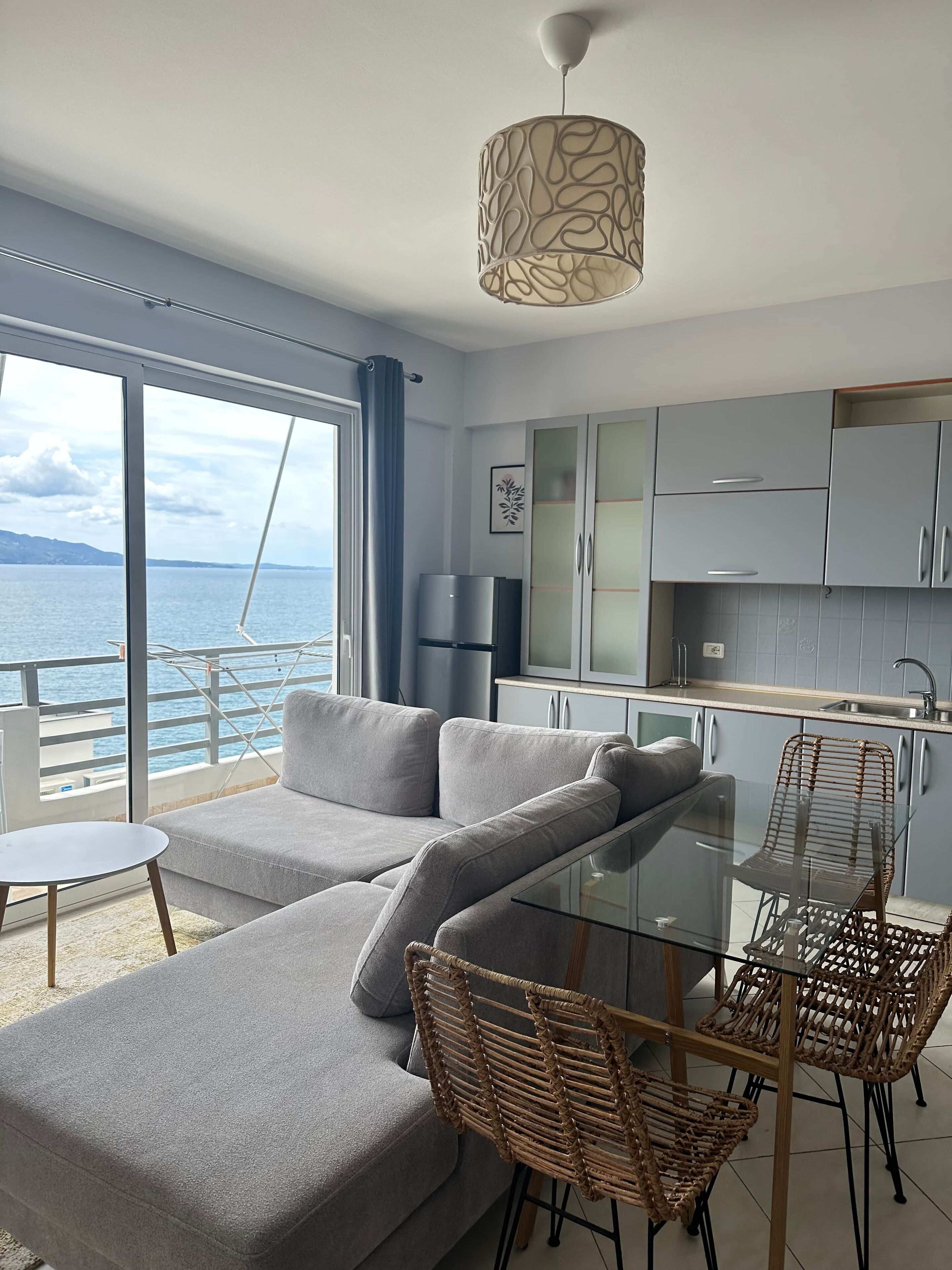 Ein modernes Wohnzimmer mit einer Couch, einem Glastisch, Korbstühlen und Meerblick.