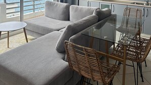 Una sala de estar moderna con un sofá, una mesa de vidrio, sillas de mimbre y vista al mar.