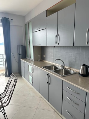 A modern kitchen with grey cabinets, a stainless steel sink, and a kettle. - Emily - Bougainville Panorama (Sarandë)