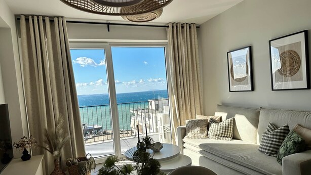 Een ruime woonkamer met een balkon met uitzicht op zee, een bank, een salontafel en decoratieve objecten.