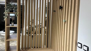 Een moderne kamer met een ingebouwde houten bank, verticale latten en uitzicht op een eetgedeelte met planten.