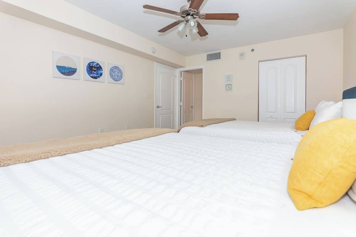 A bedroom with two beds, a ceiling fan, and wall art.