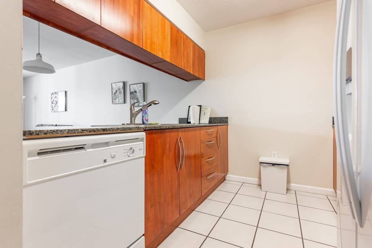 A kitchen with wooden cabinets, a white dishwasher, and a small trash bin.