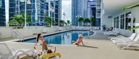 A rooftop pool area with lounge chairs and a swimming pool, surrounded by high-rise buildings.