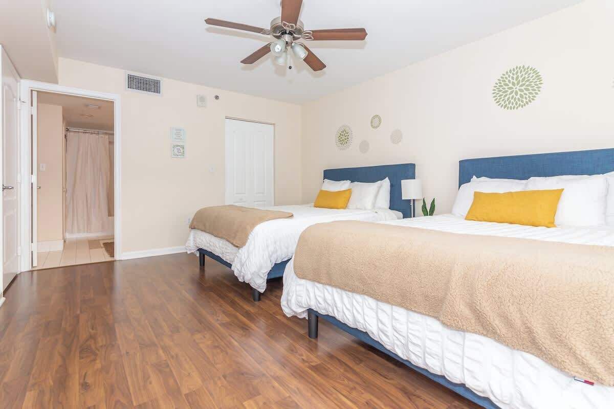 A hotel room with two beds, a ceiling fan, wooden flooring, and a door leading to a bathroom.