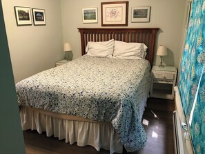 Un dormitorio con una cama grande, dos mesitas de noche, un cabecero de madera y tres cuadros enmarcados en la pared.
