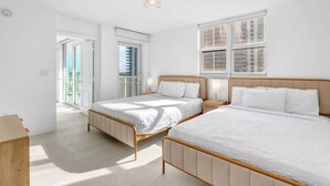 Een lichte, witte kamer met twee bedden, een groot raam en een balkon.