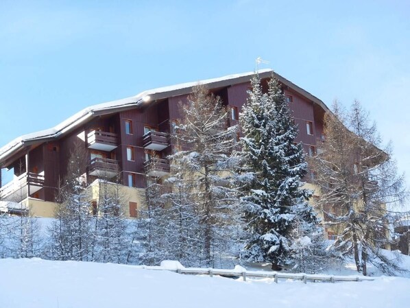Ein mehrstöckiges Gebäude mit Balkonen, umgeben von schneebedeckten Bäumen und einem klaren Himmel.