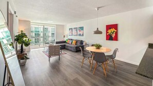 A modern living room with a sofa, dining table, and chairs, a balcony with a view, and artwork on the walls. - 1BR Brickell High-Rise Condo - Balcony & Parking (Miami)