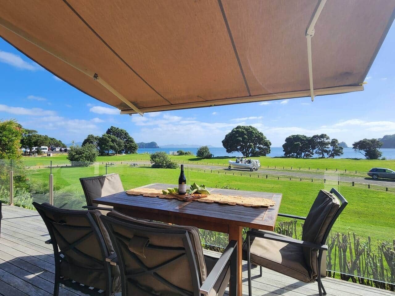 A wooden deck with a table and chairs, overlooking a grassy area and a body of water.