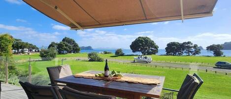 A wooden deck with a table and chairs, overlooking a grassy area and a body of water.