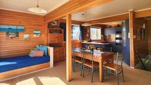 A cozy cabin interior with a wooden dining area, a blue sofa, and a kitchen with modern appliances. - Hahei Beachside Escape (Hahei)