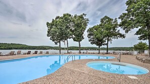 Ein Pool mit Kiesbord, umgeben von Liegestühlen und Bäumen, mit Blick auf einen See und Hügel im Hintergrund.