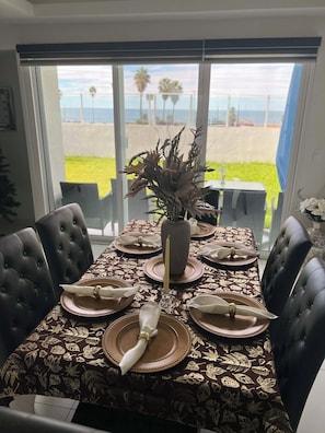 A dining table set for six with a view of the beach through large windows.