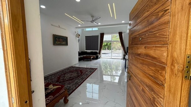 Un espacio habitable amplio con una puerta de madera, un ventilador de techo, un ventanal con cortinas, un sofá y un tapete rojo con estampado.
