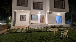 Una casa moderna de dos pisos con un césped cuidado, mobiliario exterior y una escalera visible que lleva a la entrada.