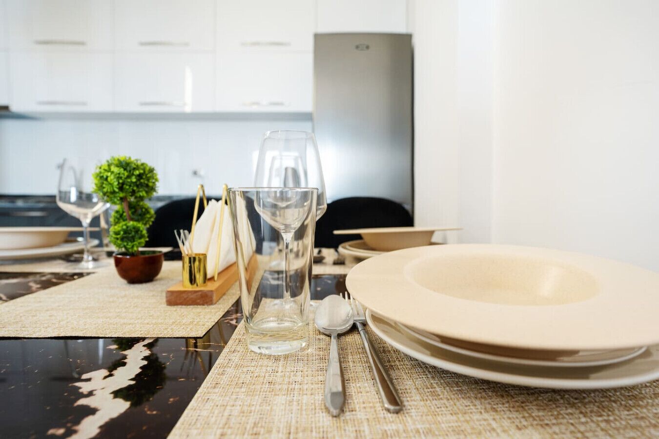 A dining table set with plates, glasses, and cutlery, with a small plant and napkin holder on the table.