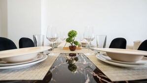 Mesa de jantar posta para seis pessoas, com copos de vidro transparentes, pratos e um pequeno vaso com planta no centro.