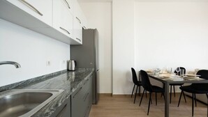Cozinha moderna com bancada de mármore, pia de aço inoxidável e geladeira. Há uma área de jantar com mesa e cadeiras.