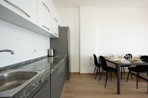 Eine moderne Küche mit Marmorarbeitsplatte, Spüle aus Edelstahl und einem Kühlschrank. Es gibt einen Essbereich mit Tisch und Stühlen.