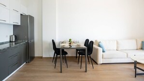 Cozinha moderna com frigorífico embutido, mesa de jantar com quatro cadeiras e sofá branco com almofadas azuis.