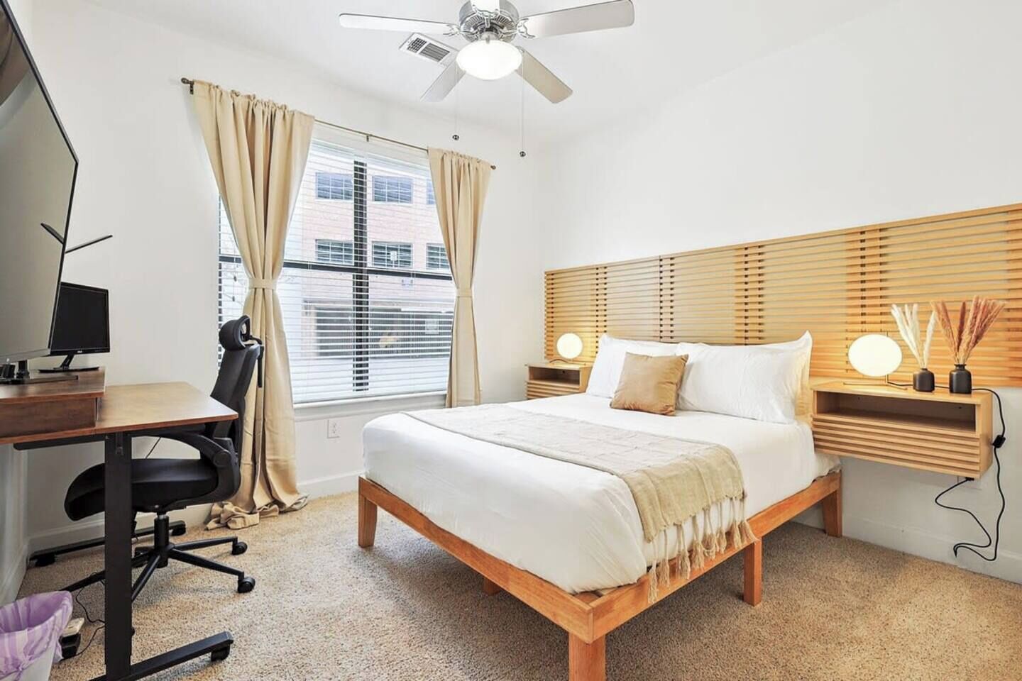 A hotel room with a bed, desk, chair, and a ceiling fan.