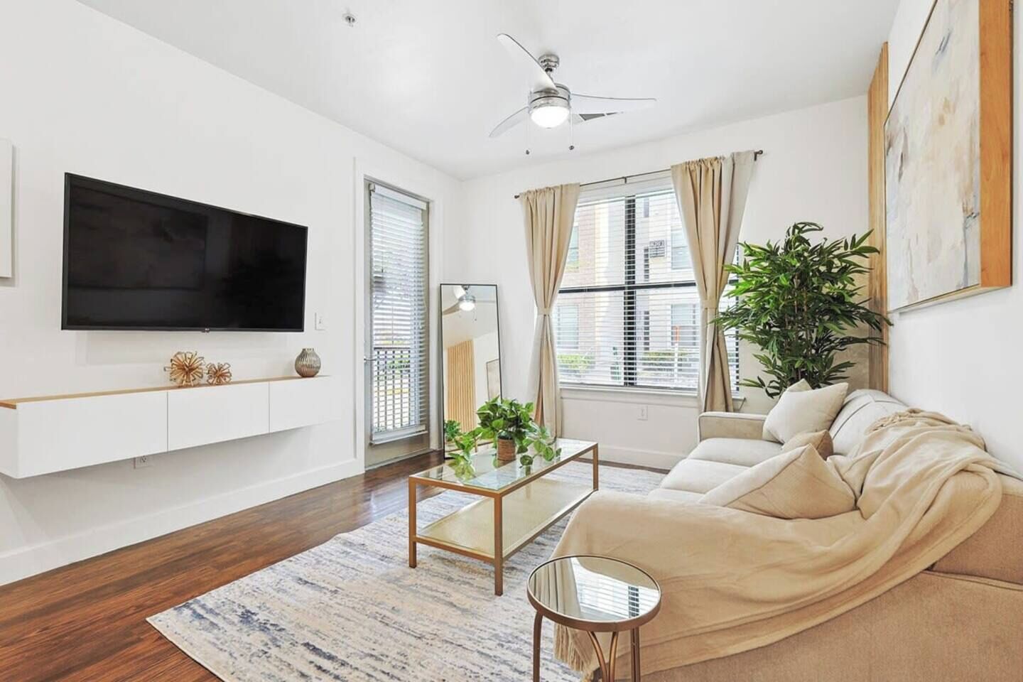 A modern living room with a flat-screen TV, a sofa, a coffee table, and a ceiling fan.