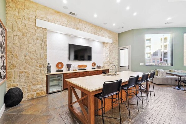 A modern kitchen with a large island, stone wall, and a flat-screen TV.