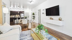 A modern living room with a sofa, coffee table, and a TV mounted on the wall. - Zen 2B2B Next to Legacy West (Frisco)