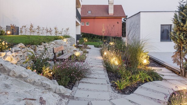 Una casa moderna con un camino de piedra que lleva a la entrada, rodeada de jardines cuidados y un cielo despejado.